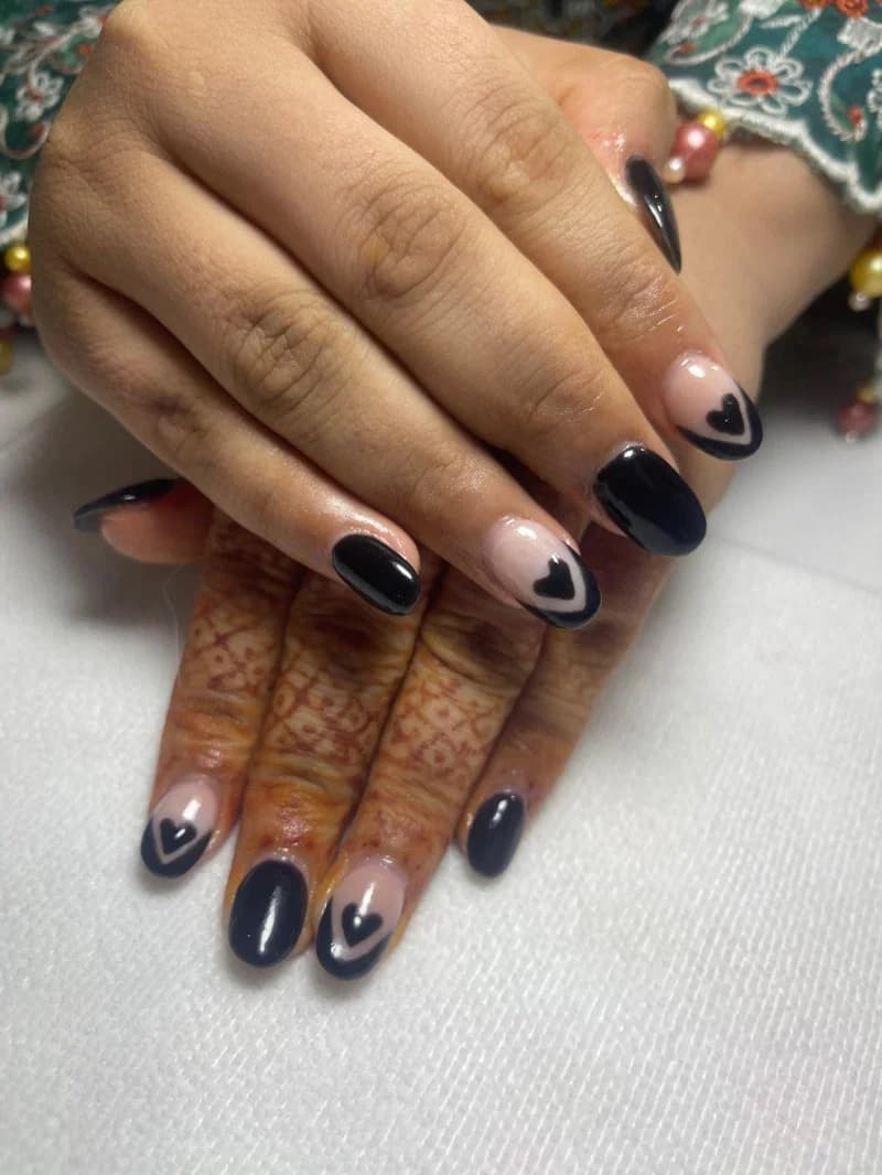 Glossy black gel nails with nude accents and tiny black hearts, over faded henna