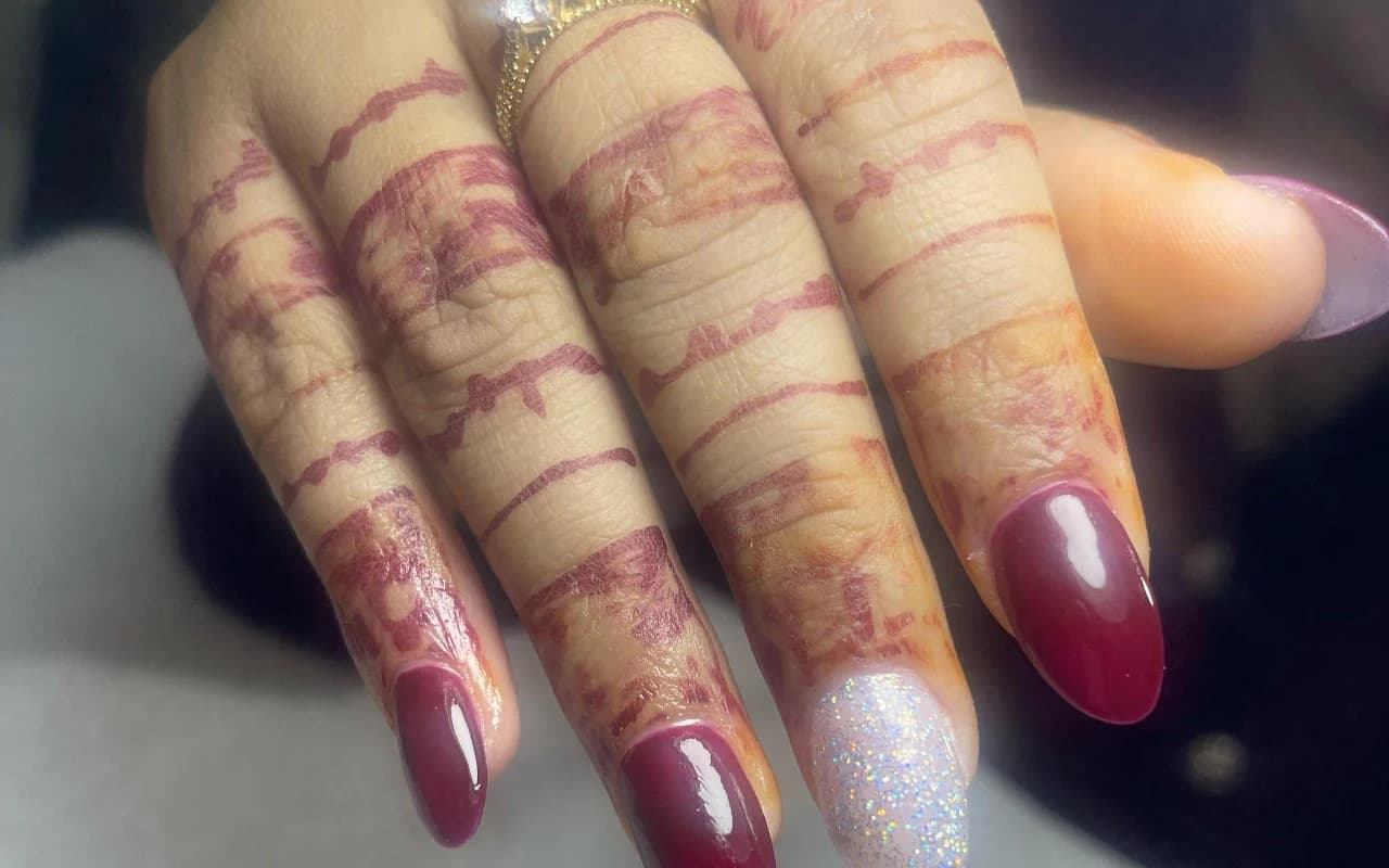 Deep burgundy almond gel nails with a glitter accent, finished alongside fresh henna