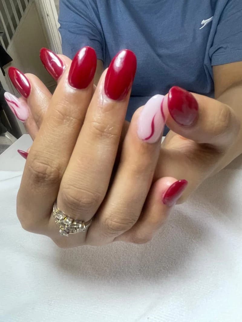 Glossy cherry-red almond nails with a red-and-white swirl accent nail