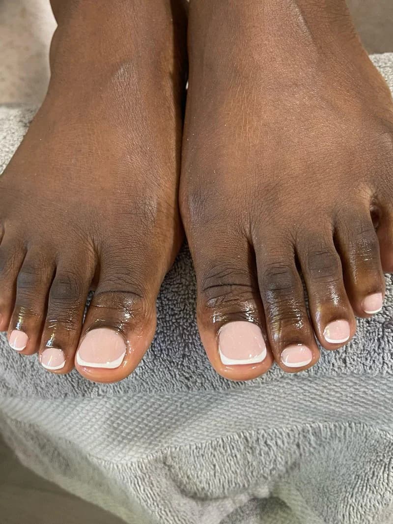 Fresh French pedicure with crisp white tips, resting on a grey towel