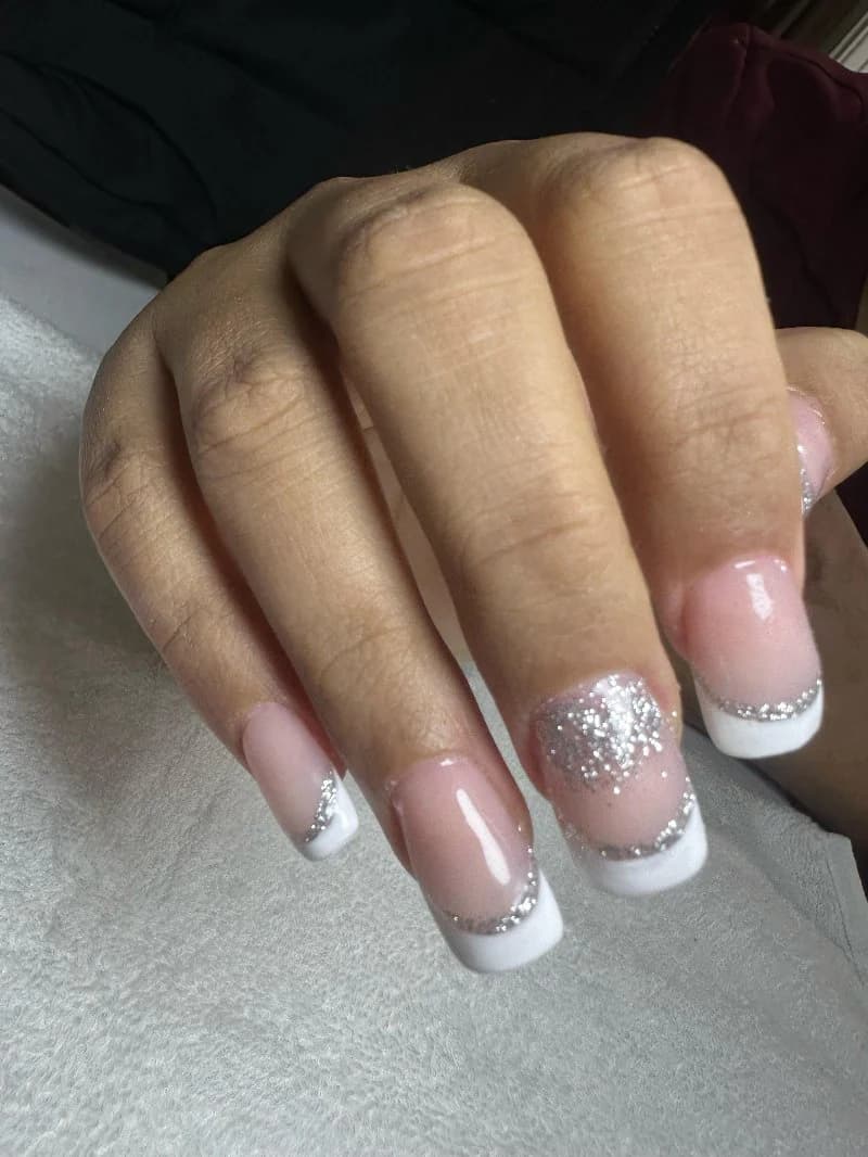 Sheer nude nails with silver glitter tips and a single white French accent