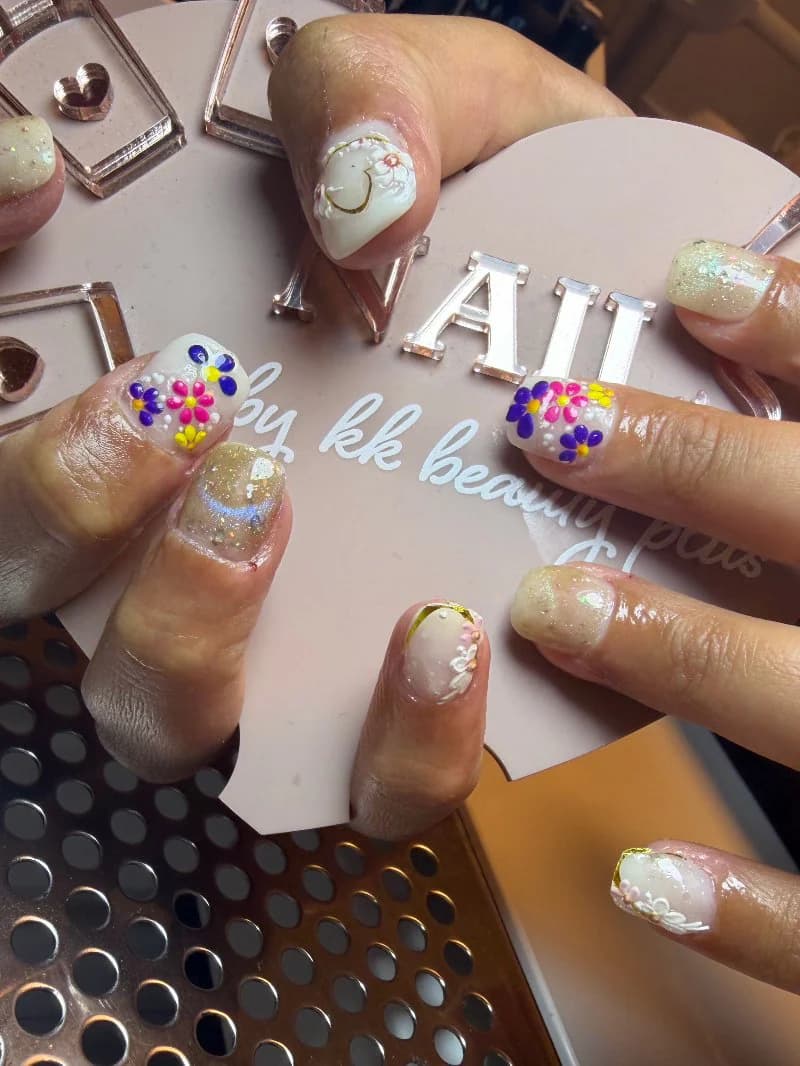 Playful nail art with hand-painted flowers, glitter and a smiley face