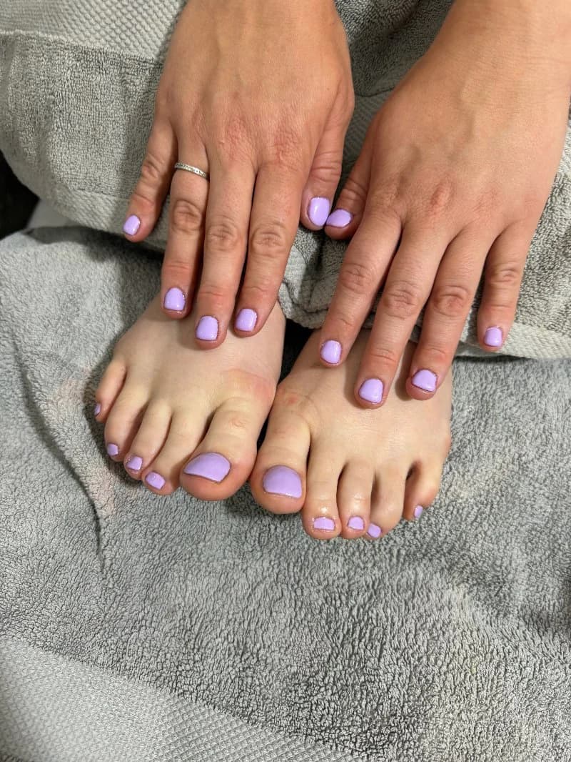 Matching lilac manicure and pedicure on a grey towel