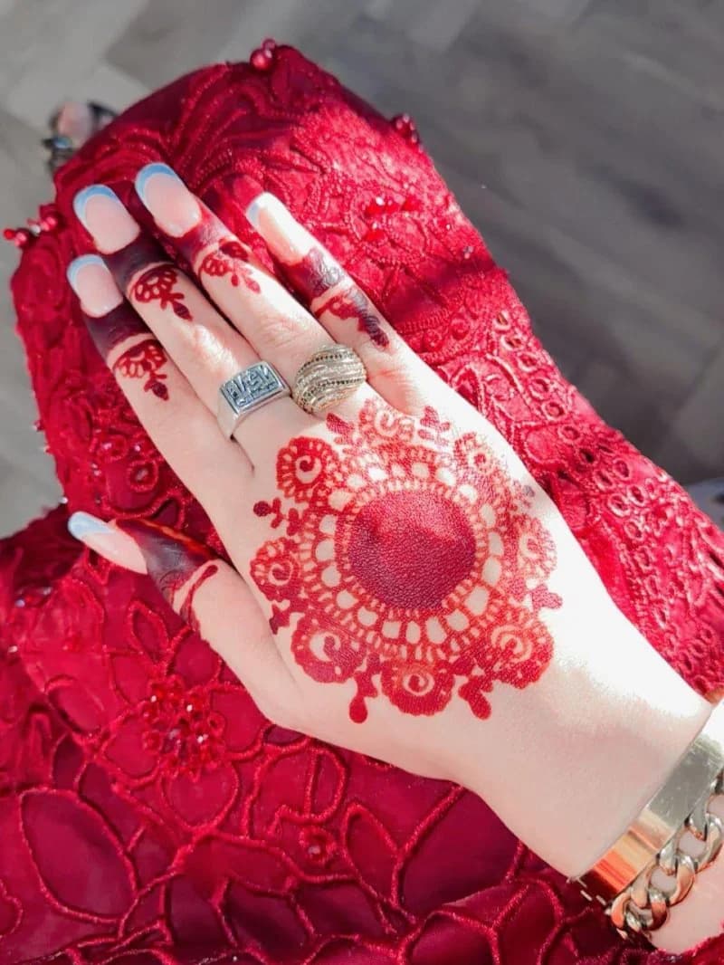 Red bridal henna with a bold mandala on the back of the hand and lace-edged sleeves