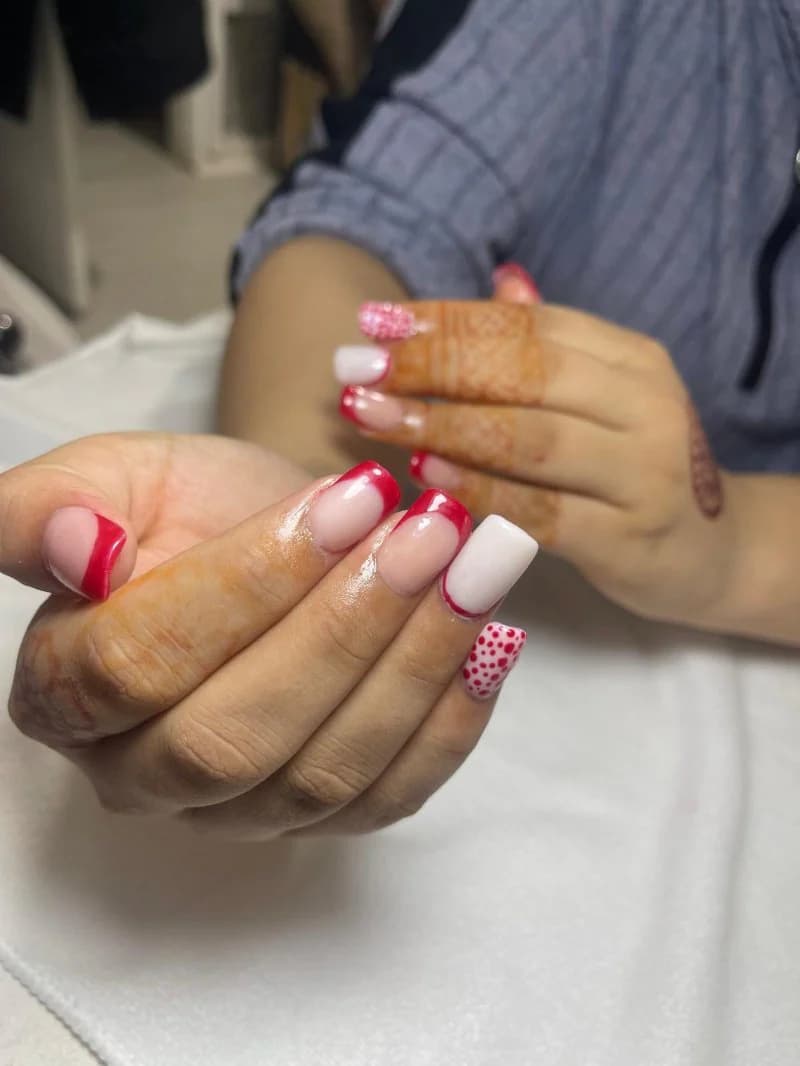 Red and white French tips with a polka-dot accent nail, shown off mid-appointment