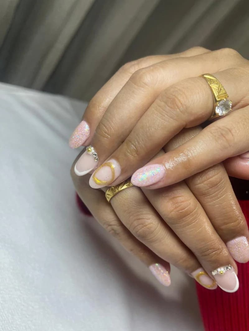 Sheer pink almond nails with a fine gold line and glitter accents