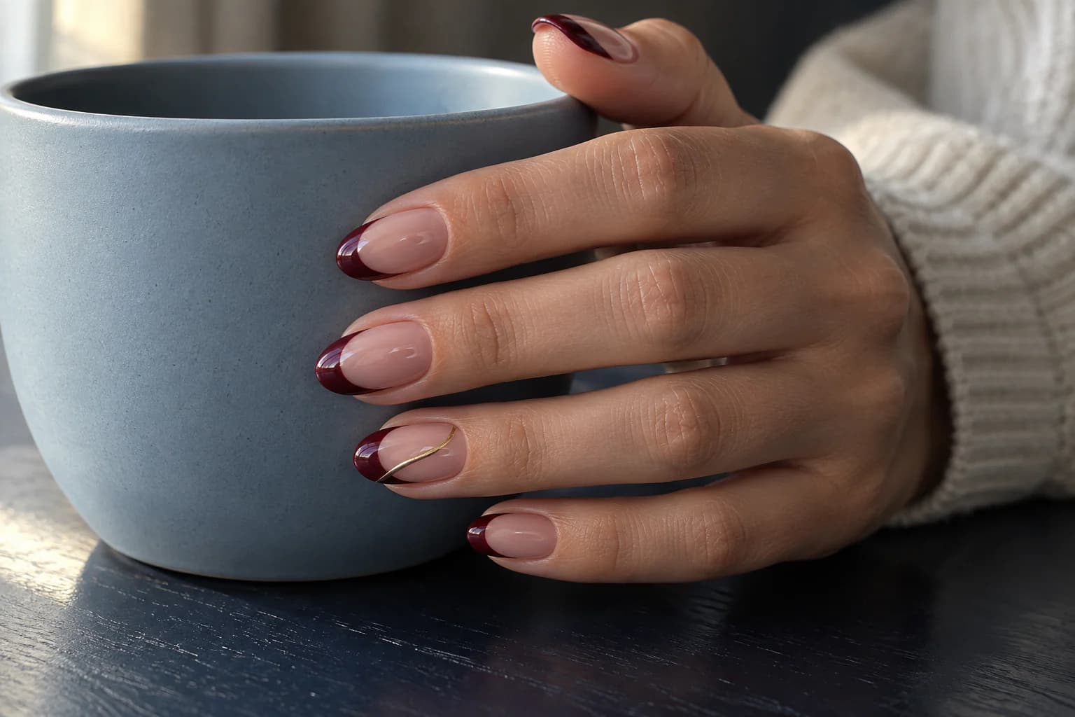 Burgundy French curves with a fine gold accent on almond gel nails